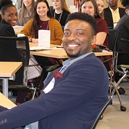 Male professional wearing a suit and bow tie, sitting a desk learning and smiling. 