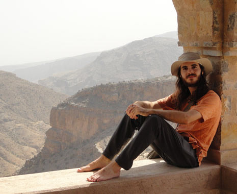 Young man sits in an open stone archway with a mountainous backdrop