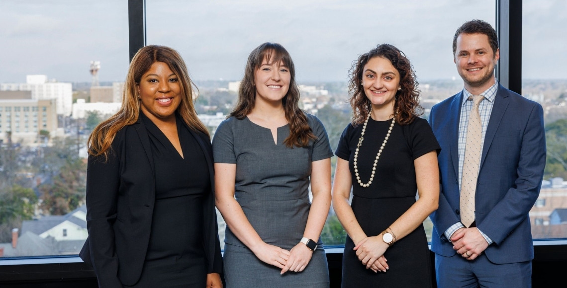 The USC representatives from the Lewis-Burke Associates pose in front of a window overlooking Columbia.