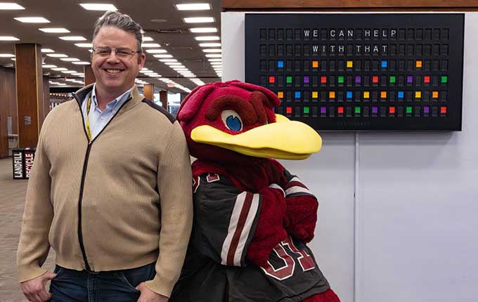 Cocky and Librarian in Thomas Cooper Library in front of sign that reads, 