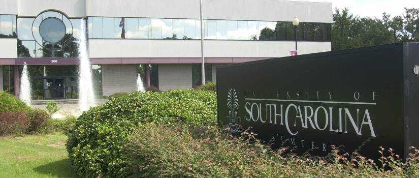 Large sign that reads "University of South Carolina Sumter" surrounded by shrubbery in front of a campus building