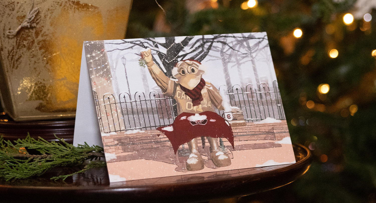 The 2025 holiday card sits on a table in the President's House next to a small gold basket and greenery