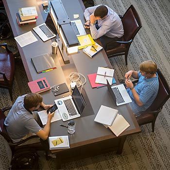 View of a study table from above with several students gathered around with laptops and notebooks.