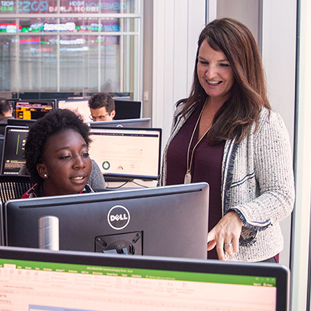 Porfessor talking with a student in a computer lab. 