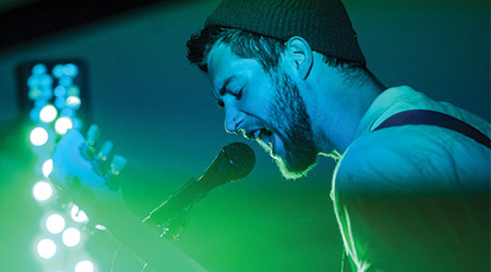 A singer singing into a microphone with blue and green stage lights signing on him. 