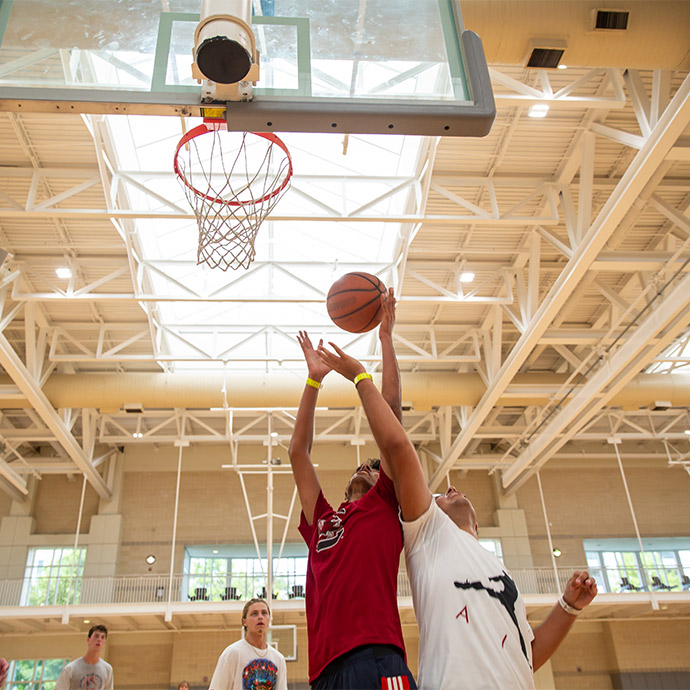 Two students going head to head under the basketball goal shooting the ball. 