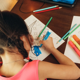 A young girl wearing pig tails and a pink shirt colors with markers and colored pencils