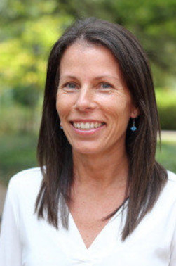 Kimberly Becker wears a white shirt and smiles at the camera from in front of an out-of-focus green background.