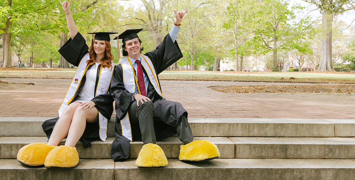 Students sitting on horseshoe in graduation regalia and Cocky shoes