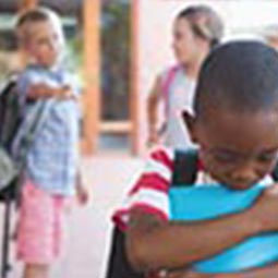 a pair of white children point teasingly at a sad black child in the foreground 