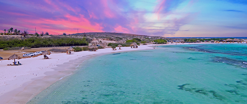 An aerial view of beaches in Aruba with the sun setting in the background.