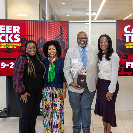 Four professionals pose together at a Career Tracks event, standing in front of garnet and black promotional displays.