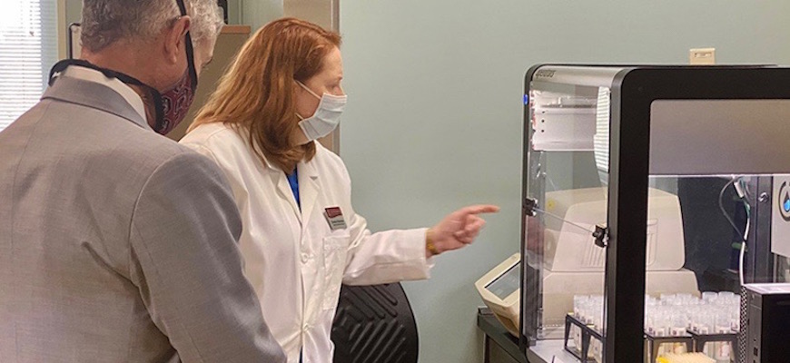 President Caslen observing lab manager, Dr. Carolyn Banister, explaining the the lab’s liquid handling robots.