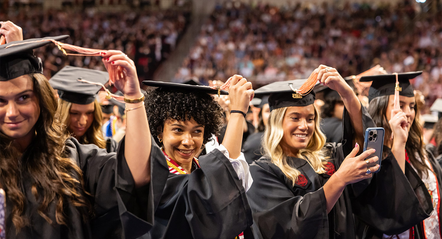 four women graduates at commencement turning tassels on their caps