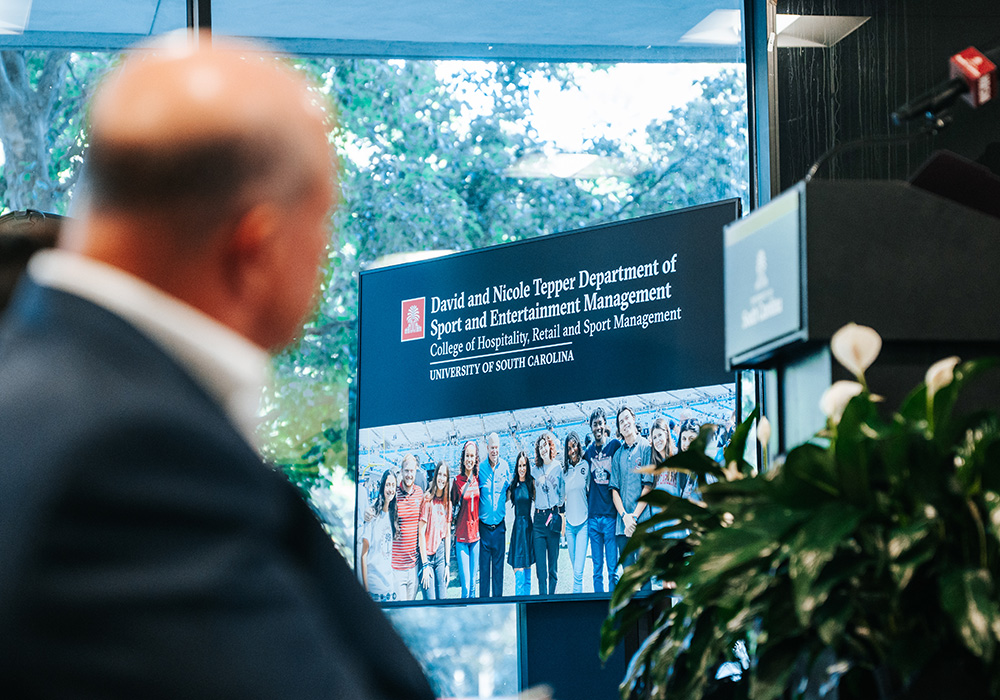 Carolina Panthers owner David Tepper looking toward video screen displaying logo and photo of students