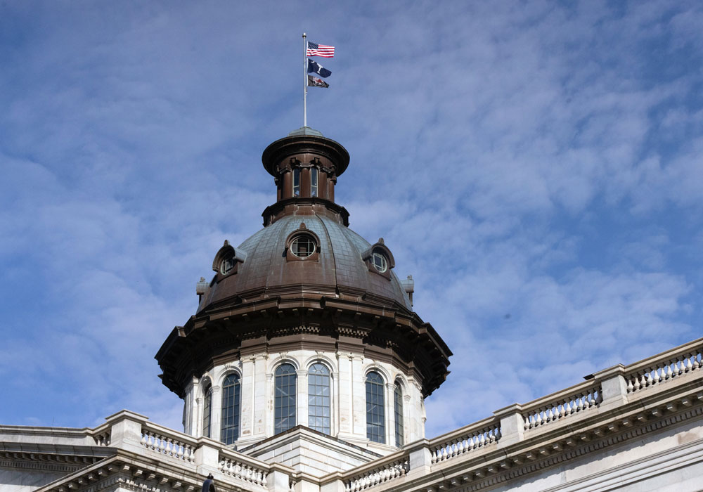 sc statehouse dome with U.S., S.C. and USC flags flying over it