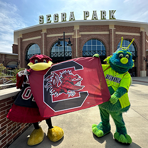 Cocky and Mason holding a Gamecock flag in front of Segra Park.