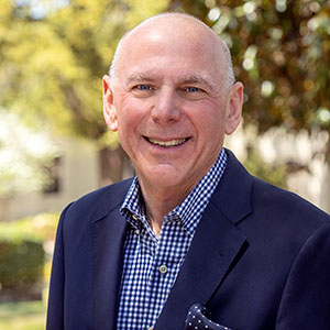 man in blue check shirt and blue jacket with trees in background