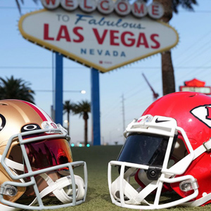 A gold helmet and a red helmet sit on the ground with a sign behind them that reads, 