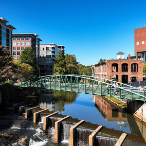 Waterfall on a city river with a bridge and buildings in the background