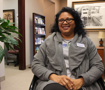 woman with dark hair and glasses wearing a gray sweater sitting in an office 